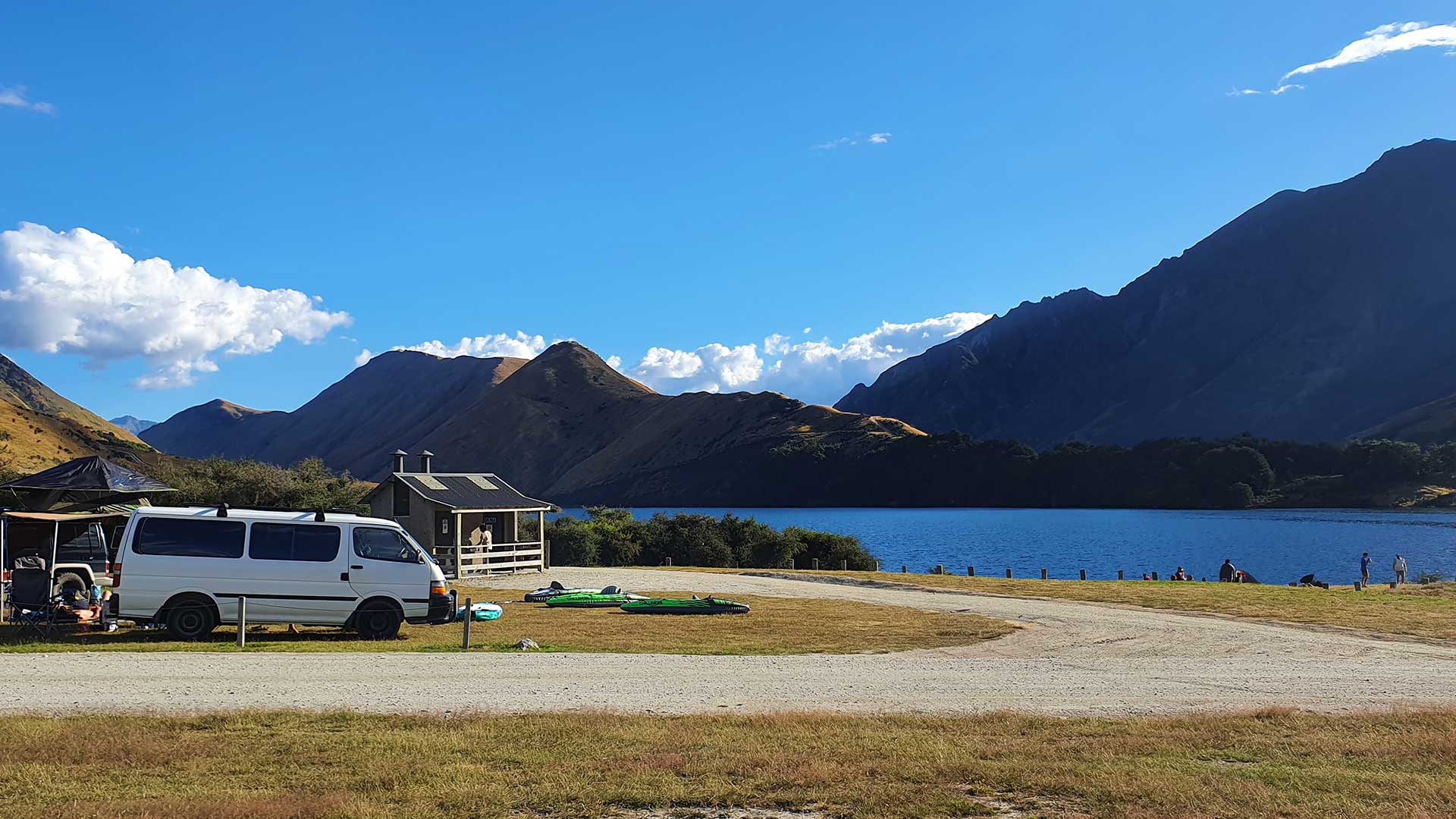 Campervans, kayaks and a small building beside Moke Lake, with mountains behind.