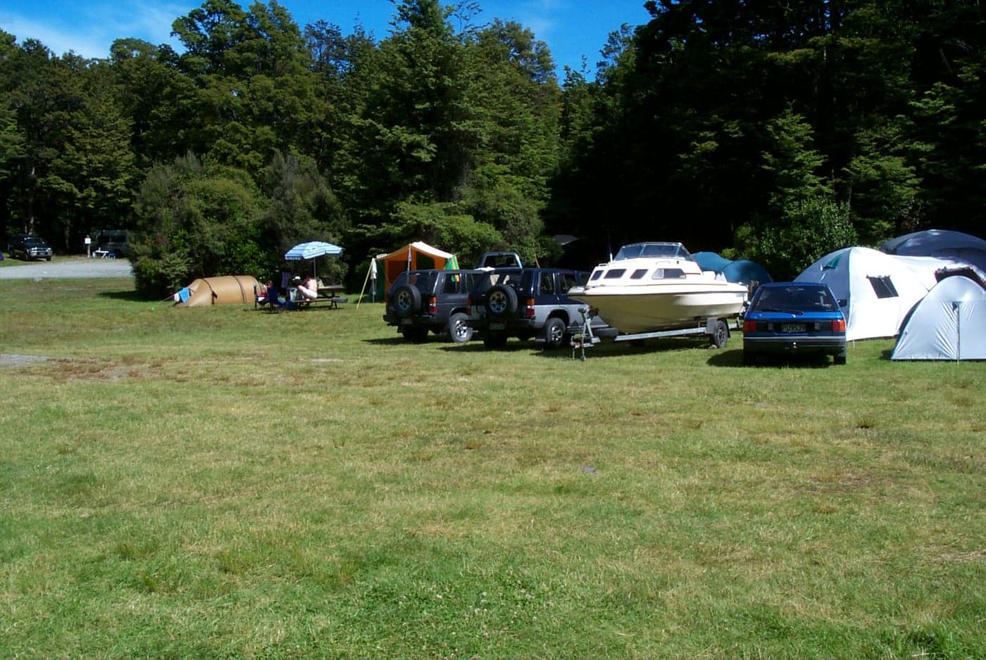 Tents, parked vehicles and a boat trailer on grassy camping pitches bordered by trees at Kerr Bay.