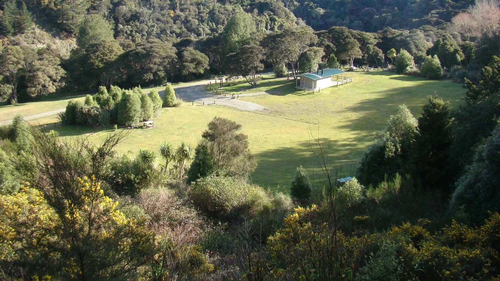 Elevated view of grass, gravel tracks, picnic tables and a green-roofed building at Glencoe Campsite.