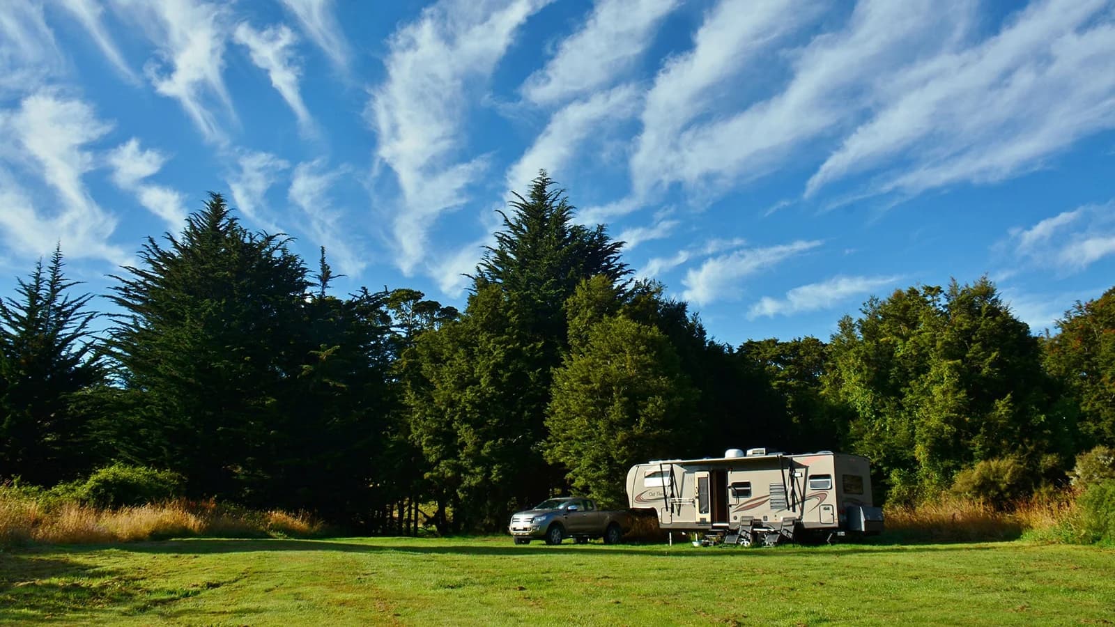 A camping vehicle and pickup parked on grass beside trees at Tawanui Campsite.