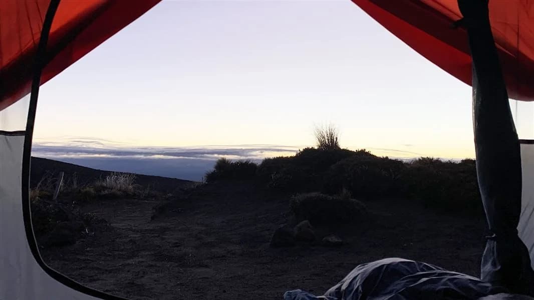 View from inside a red and cream tent out to a volcanic landscape.