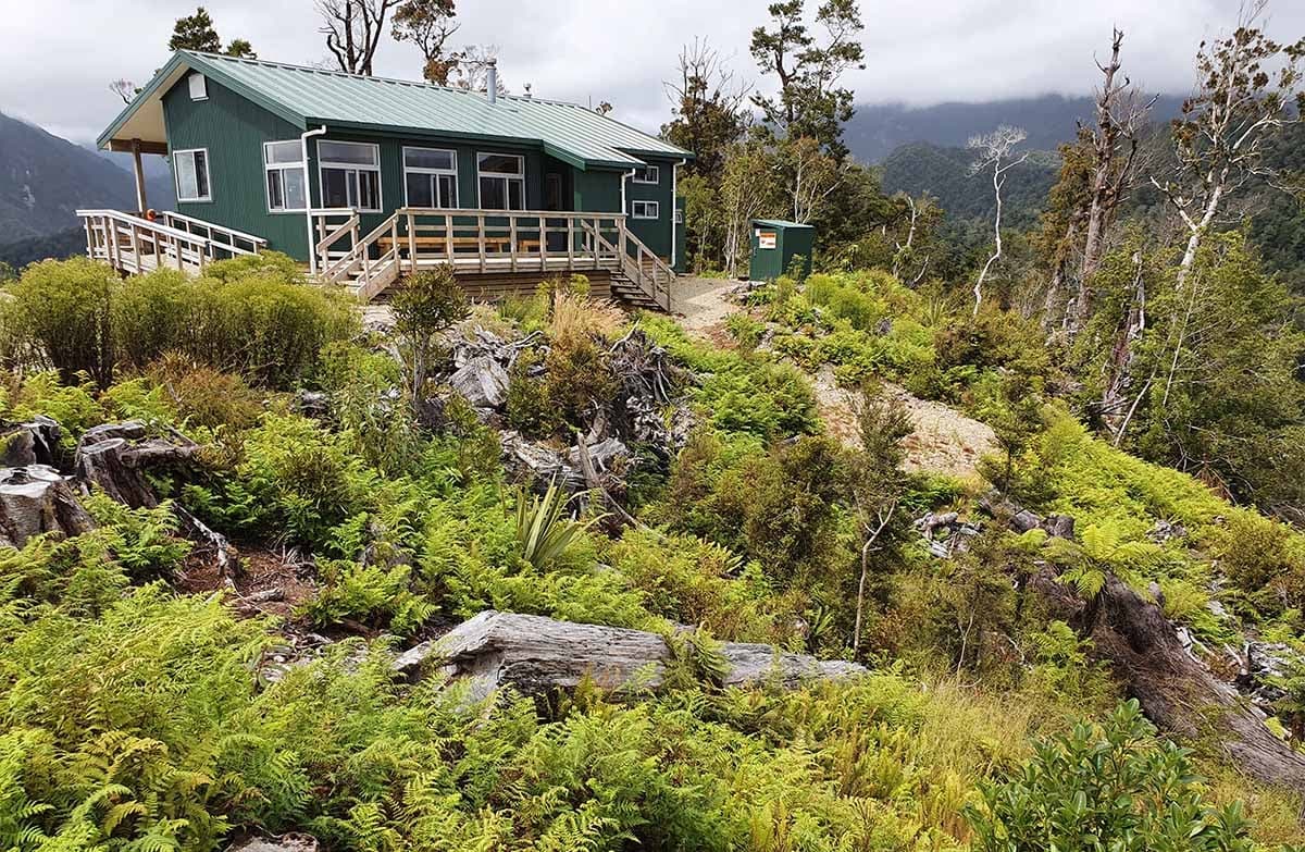 Pororari Hut viewed from the outside showing the dense scrub and mountainous terrain.