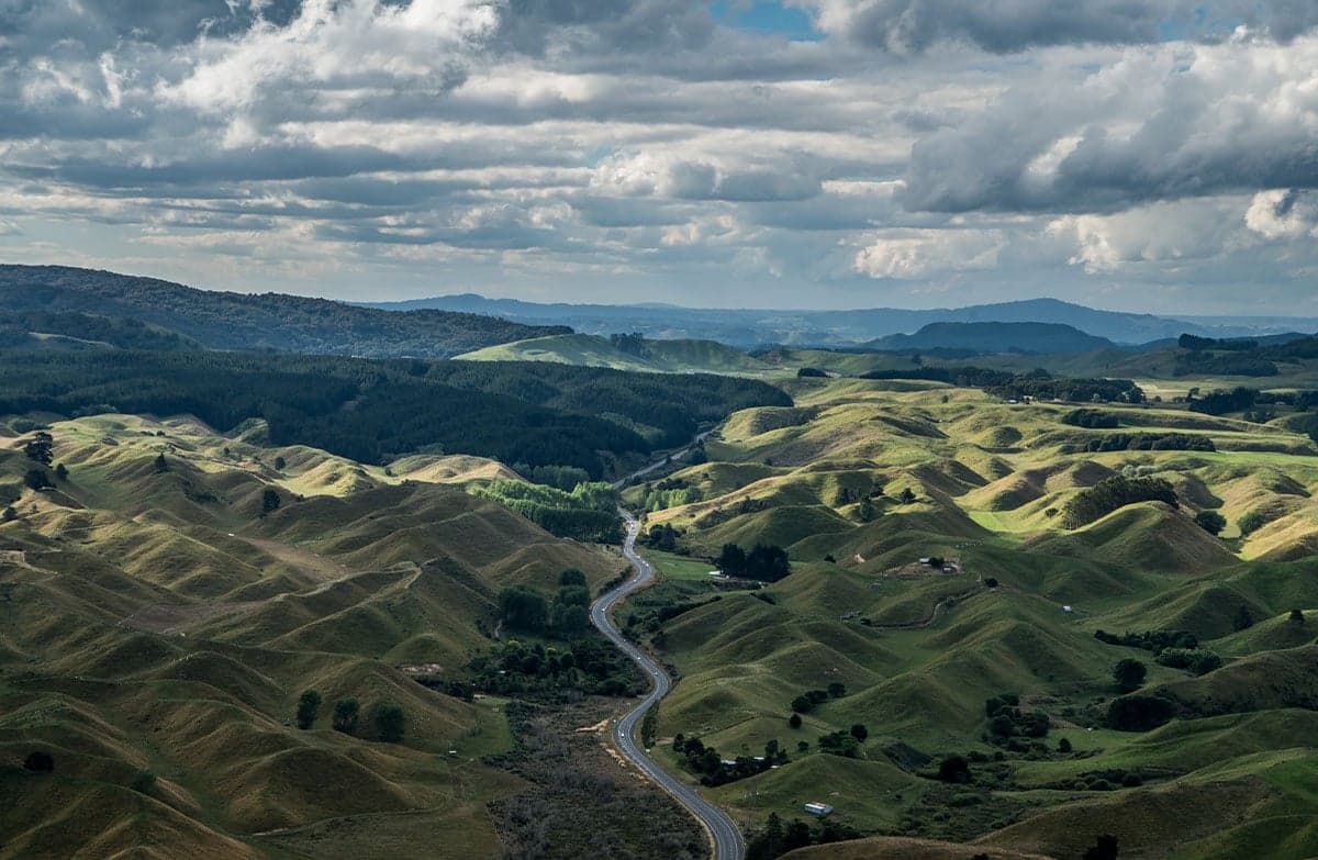 A view from an elevated position, over rolling green hills with a winding road through a valley.