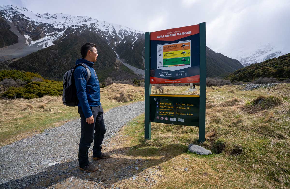 Hiker stops to read the avalanche danger information sign on the Sealy Tarns Track.
