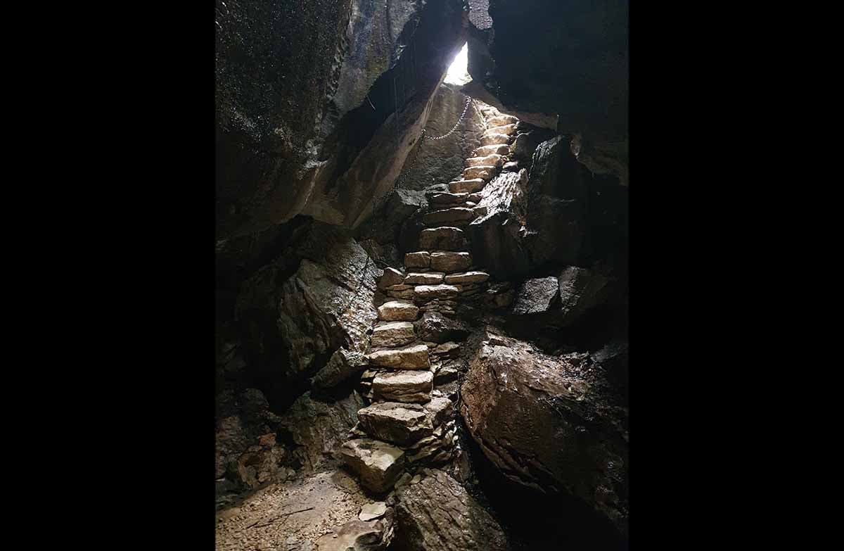 A staircase made of steps hewn from rock. There is light beaming down from outside the cave.