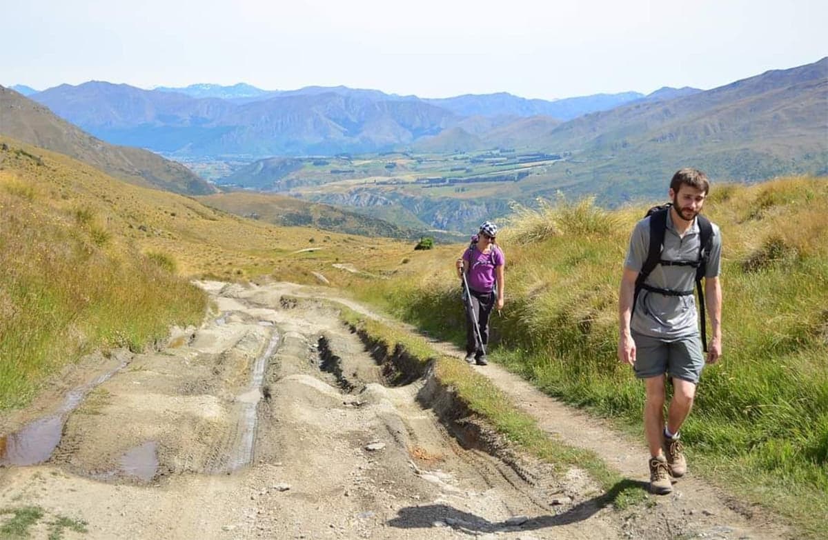 Two people walk along a bare 4WD track. Beautiful views of rolling hills can be seen in the background.