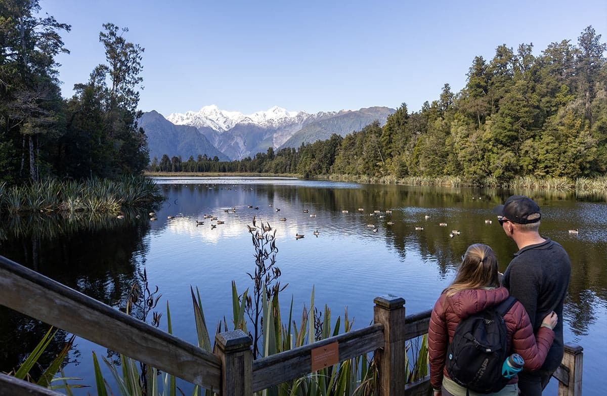Two visitors looking over a lake with Canada geese and reflections of the Southern Alps.