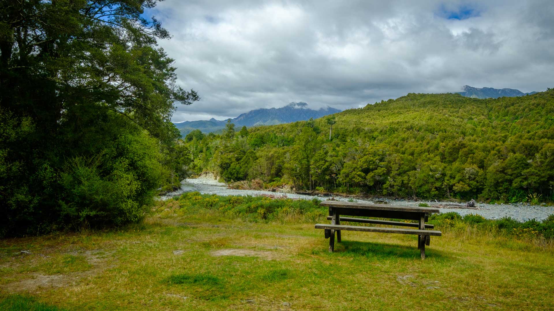 Picnic table on a grassy clearing at Brown Campsite with the river and forested hills beyond.