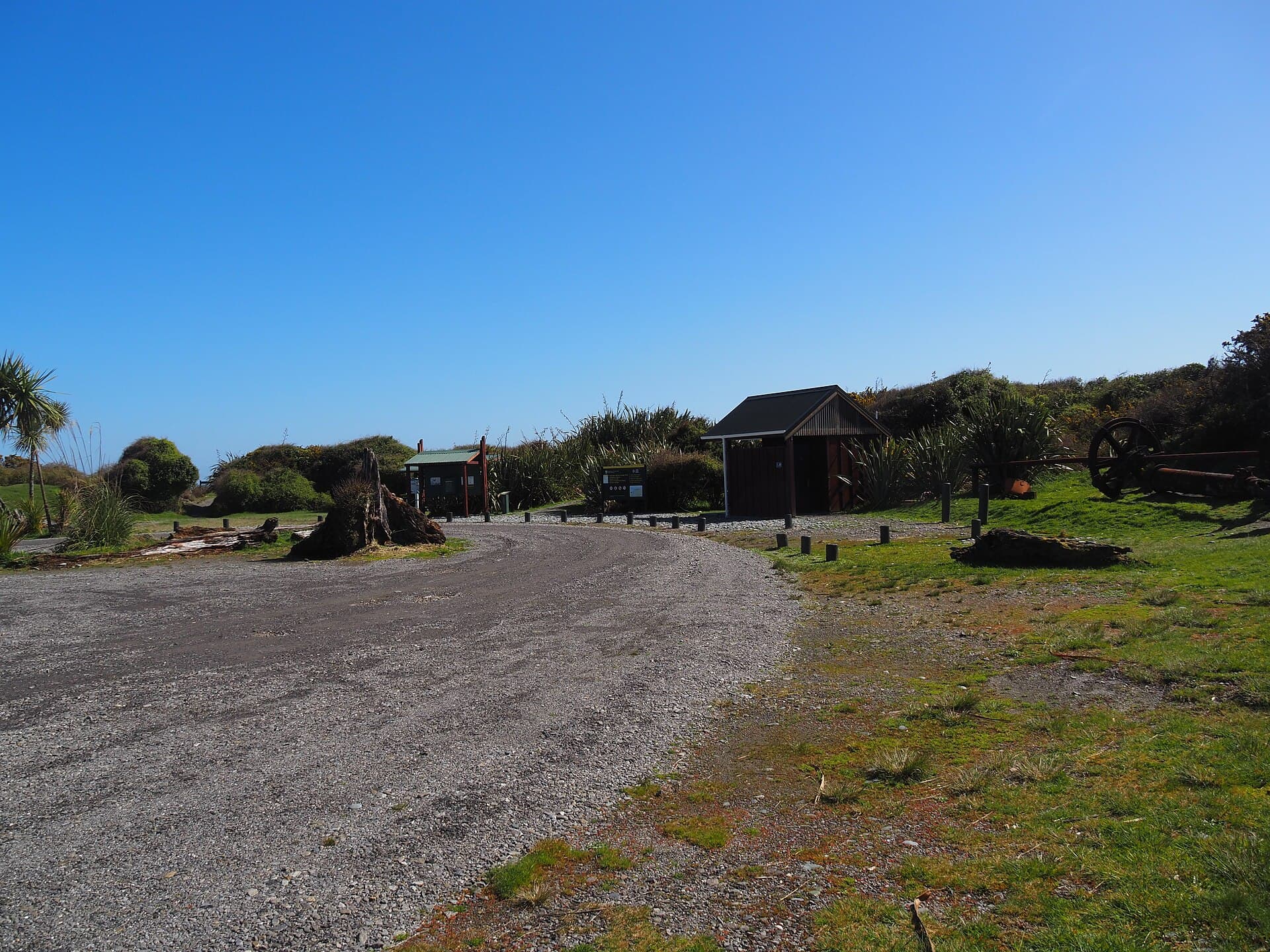 Gravel arrival area, timber buildings, information signs and low vegetation at Gillespies Beach campground.