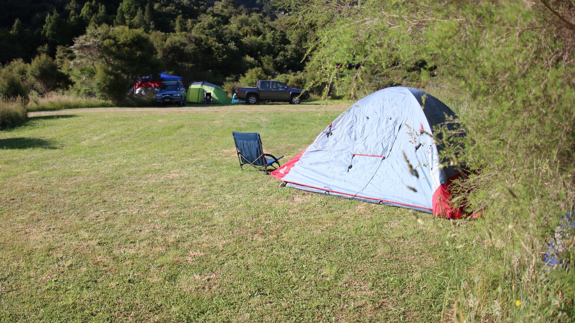 A grey and red tent, camping chair, other tents and vehicles on grass at Harvey Bay Campsite.