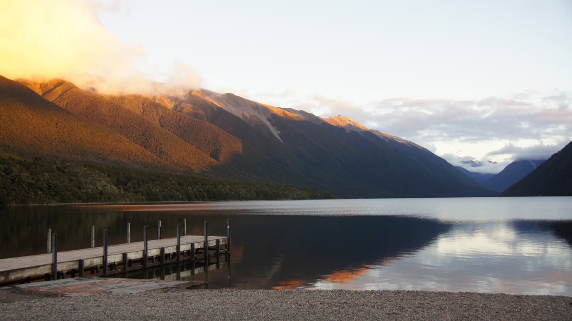 Wooden jetty, calm lake and forested mountains seen from the shore at Kerr Bay, Lake Rotoiti.