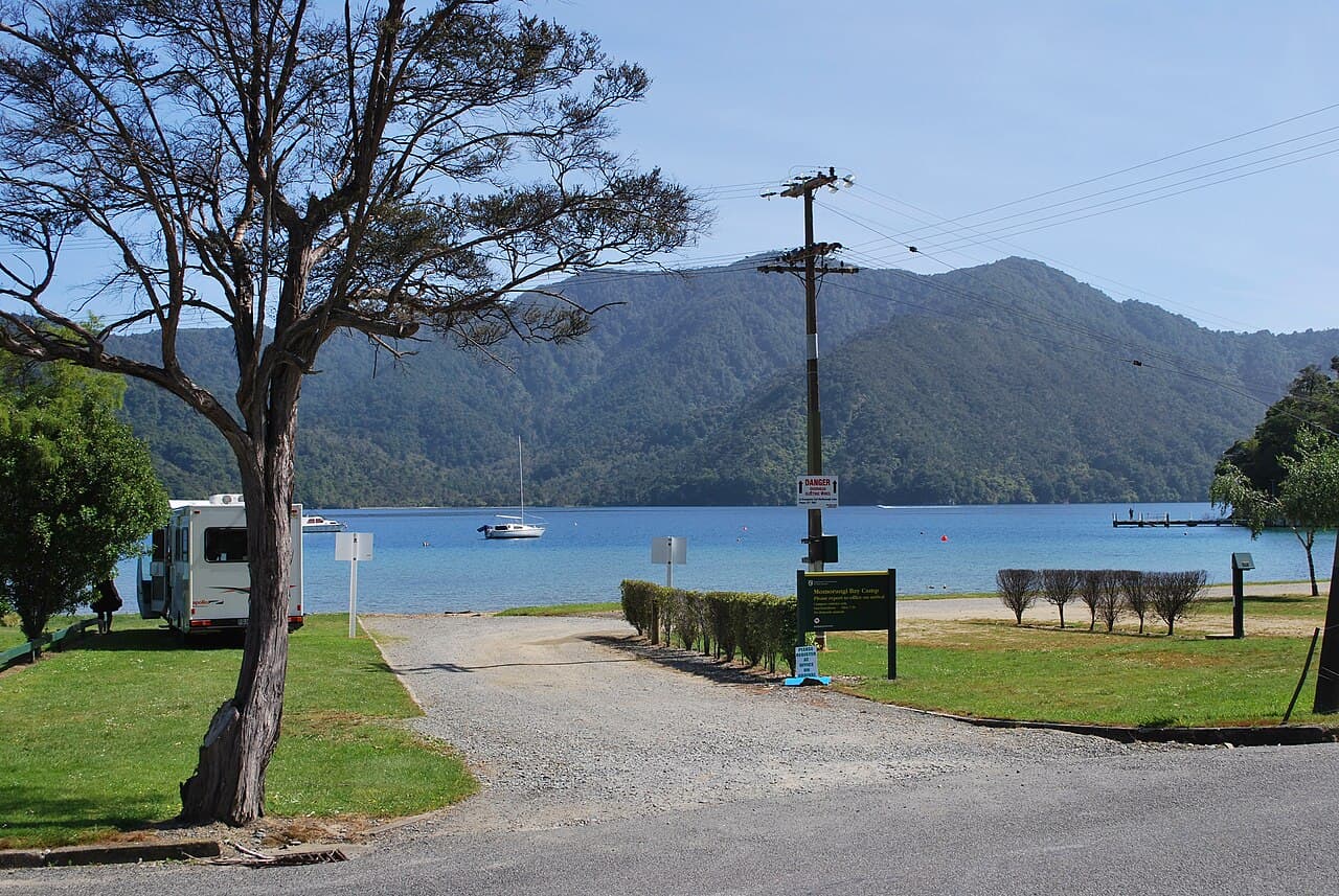 Campervan, camp sign and gravel access beside the water at Momorangi Bay Camp.