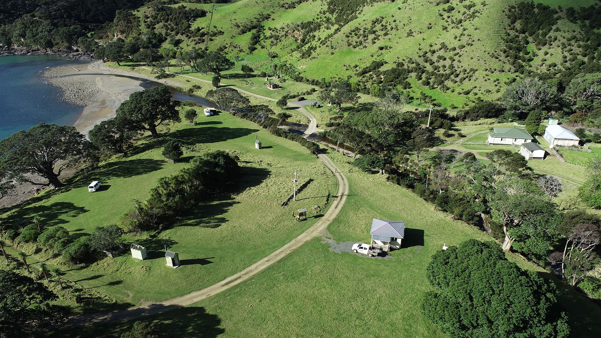 Campervans, grassy camping areas, small buildings and a winding access track beside Stony Bay.
