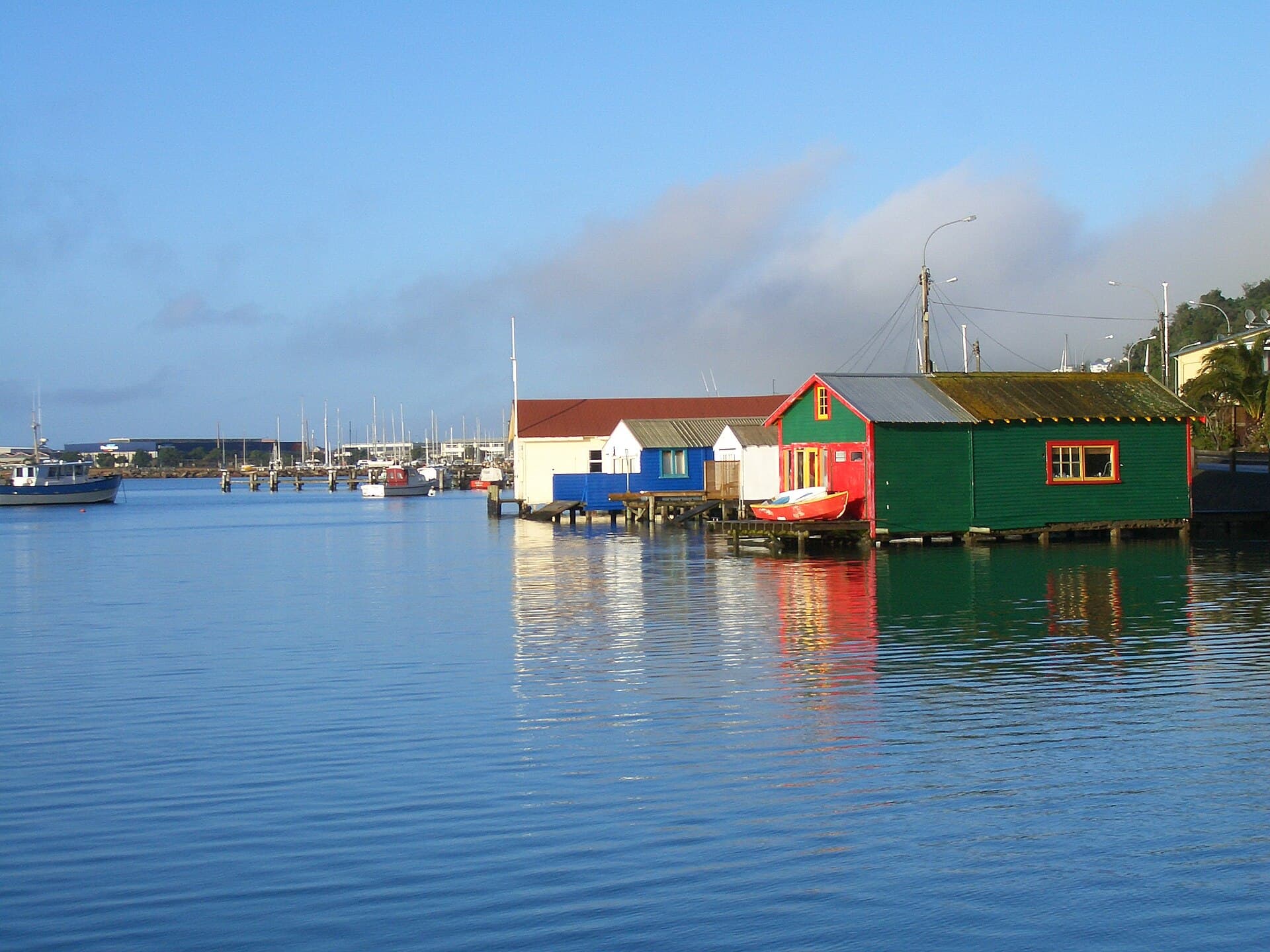 Colourful boatsheds over the water at Evans Bay, with marina masts behind them.