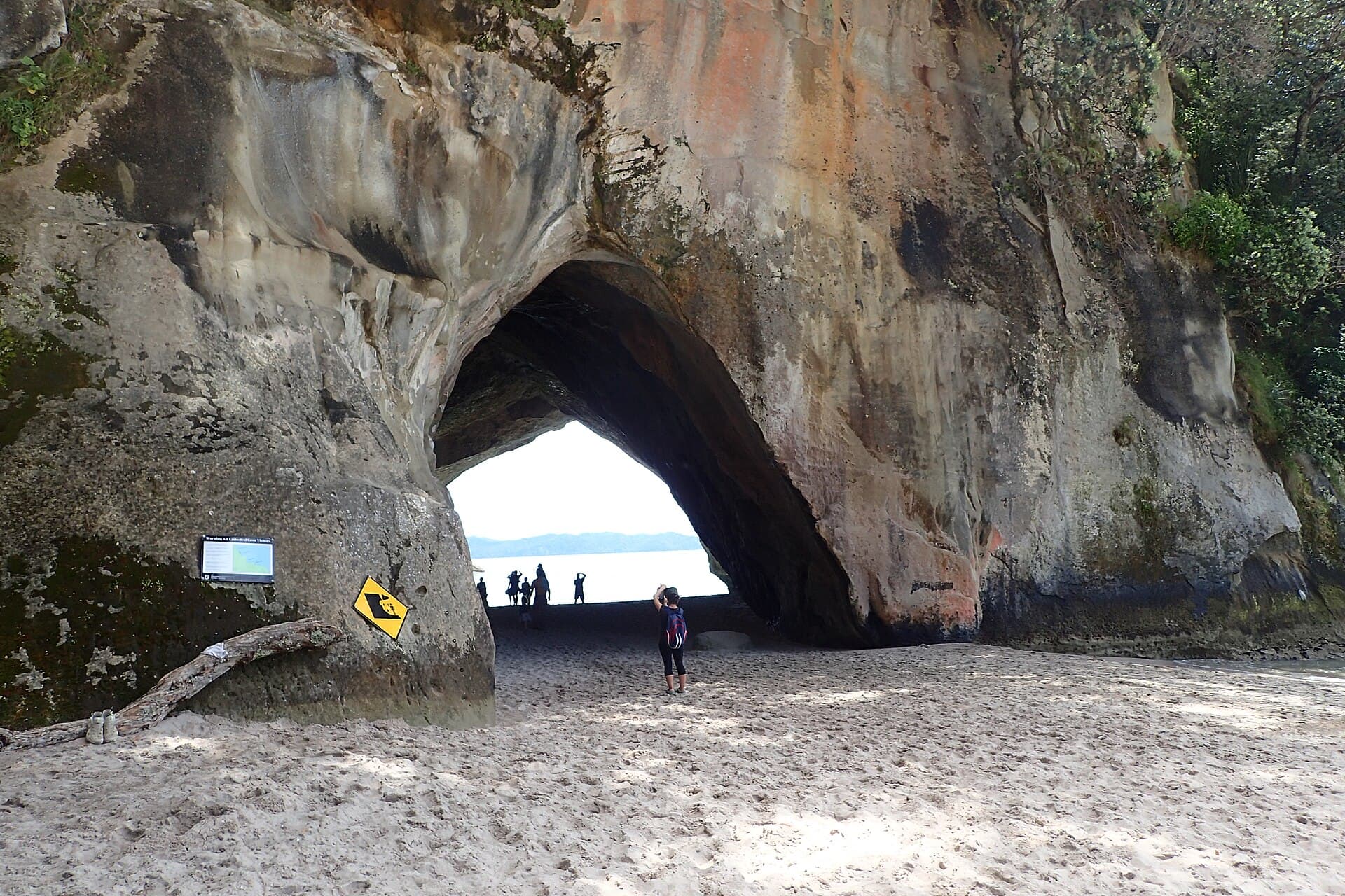 Visitors beneath Cathedral Cove's rock arch, viewed from the sand at Mare's Leg Cove.