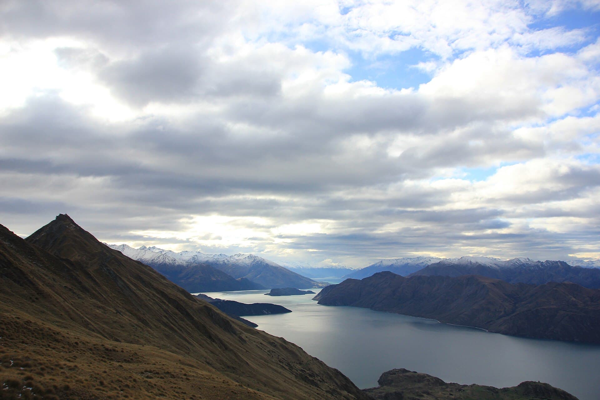 Lake Wanaka, islands and snowy distant ranges seen beyond a grassy ridge on Roys Peak.