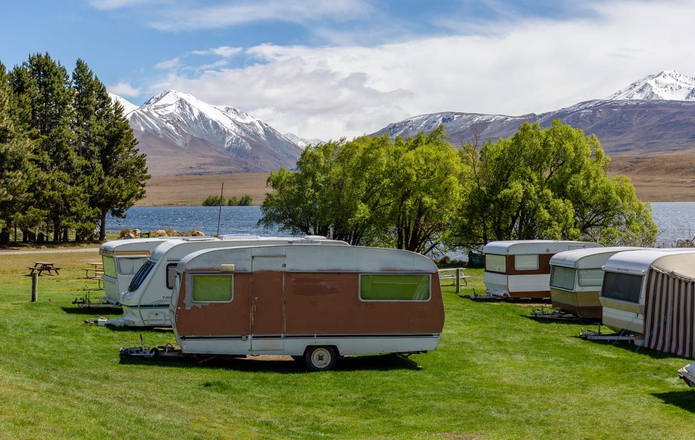 Caravans on a grassy camping area, with picnic tables, Lake Clearwater and snow-dusted mountains behind them.