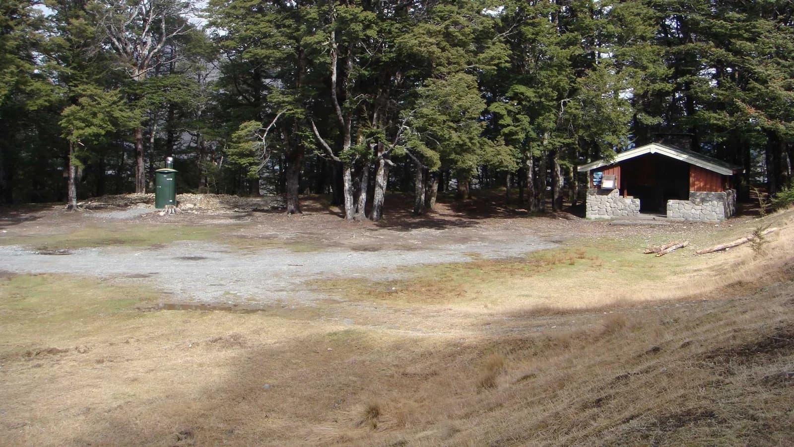 Stone-and-timber shelter, small green structure and gravel clearing at the forest edge at Hawdon Shelter Campsite.