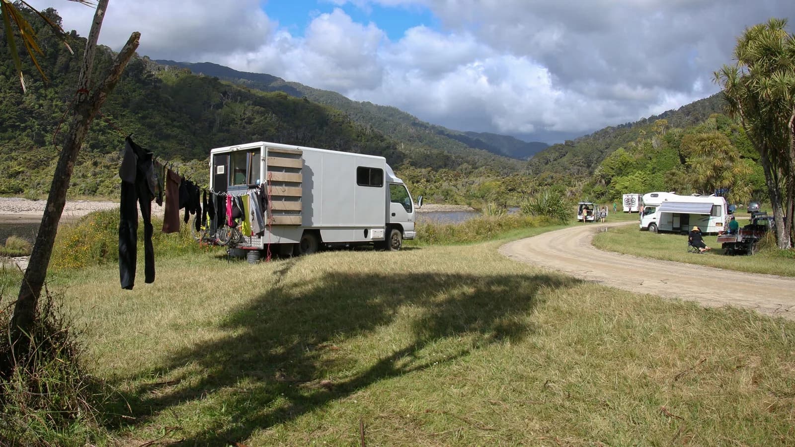 Campervans and camping vehicles beside a curving track and water at Kohaihai Campsite.