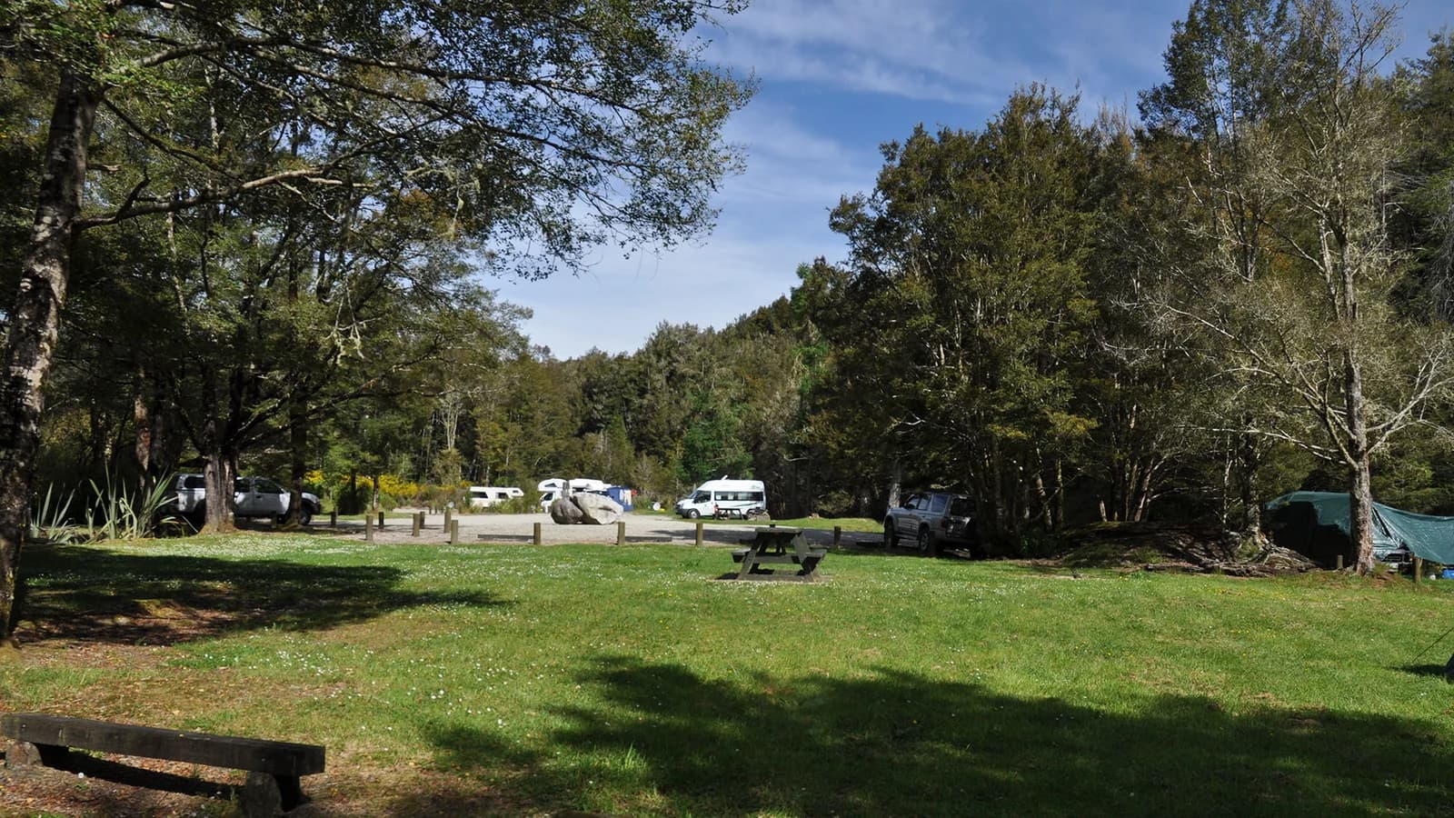Campervans, a tent, picnic tables and grassy spaces among trees at Slab Hut Creek Campsite.