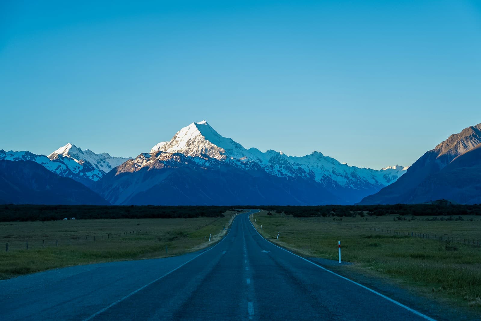 A sealed road near Glentanner leading toward snow-covered mountains beneath a clear sky.