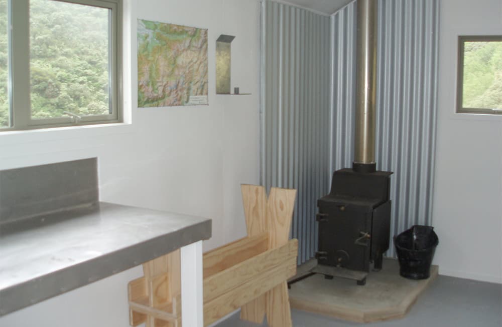 A shared metal bench, wooden seating and wood burner inside a backcountry hut.