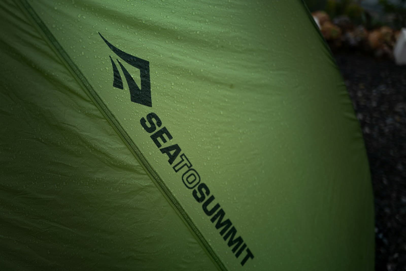 Water droplets on a green tent fly with a visible manufacturer logo.