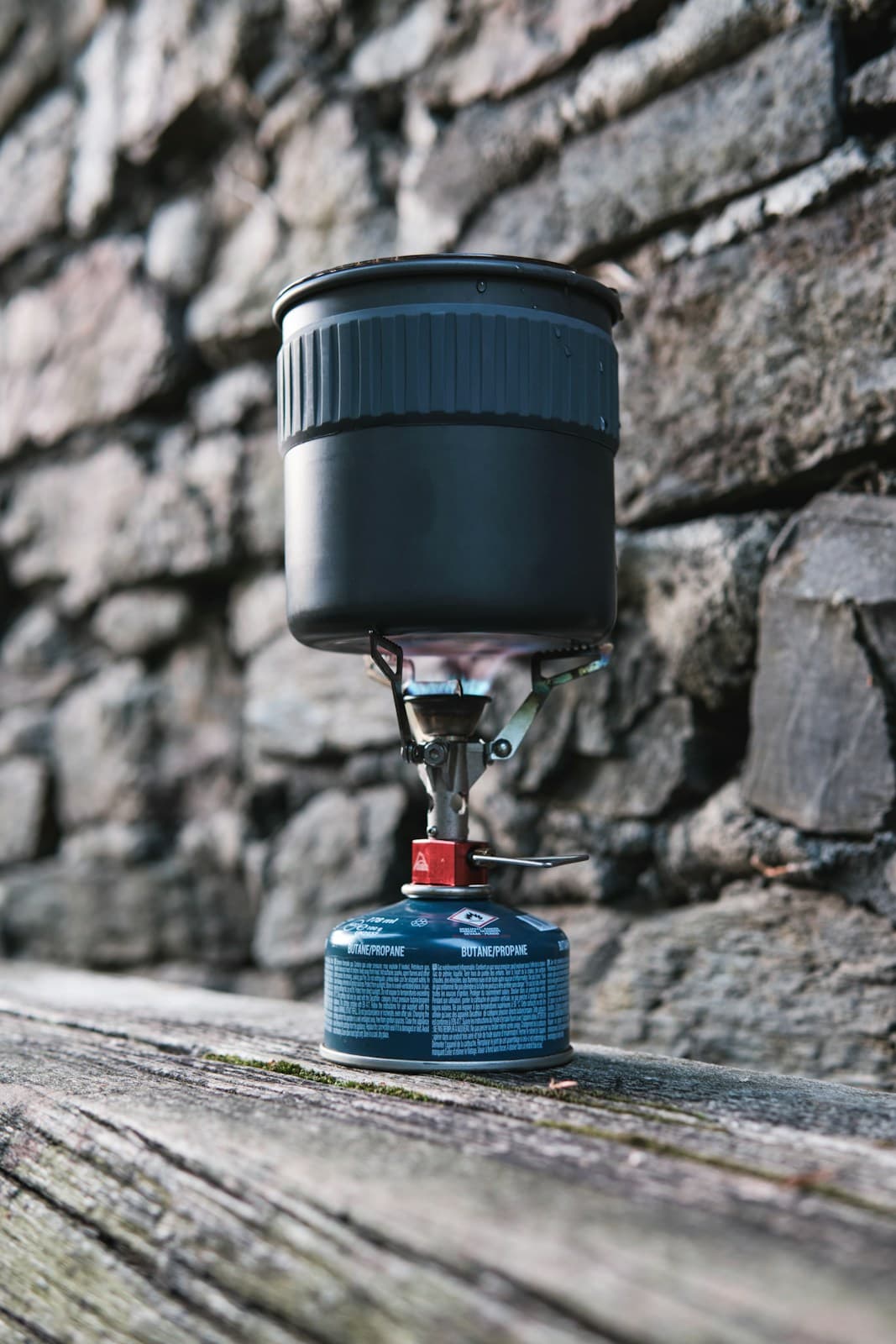 A grey cooking pot on a lit canister-mounted camping stove, with the burner and blue fuel canister visible.