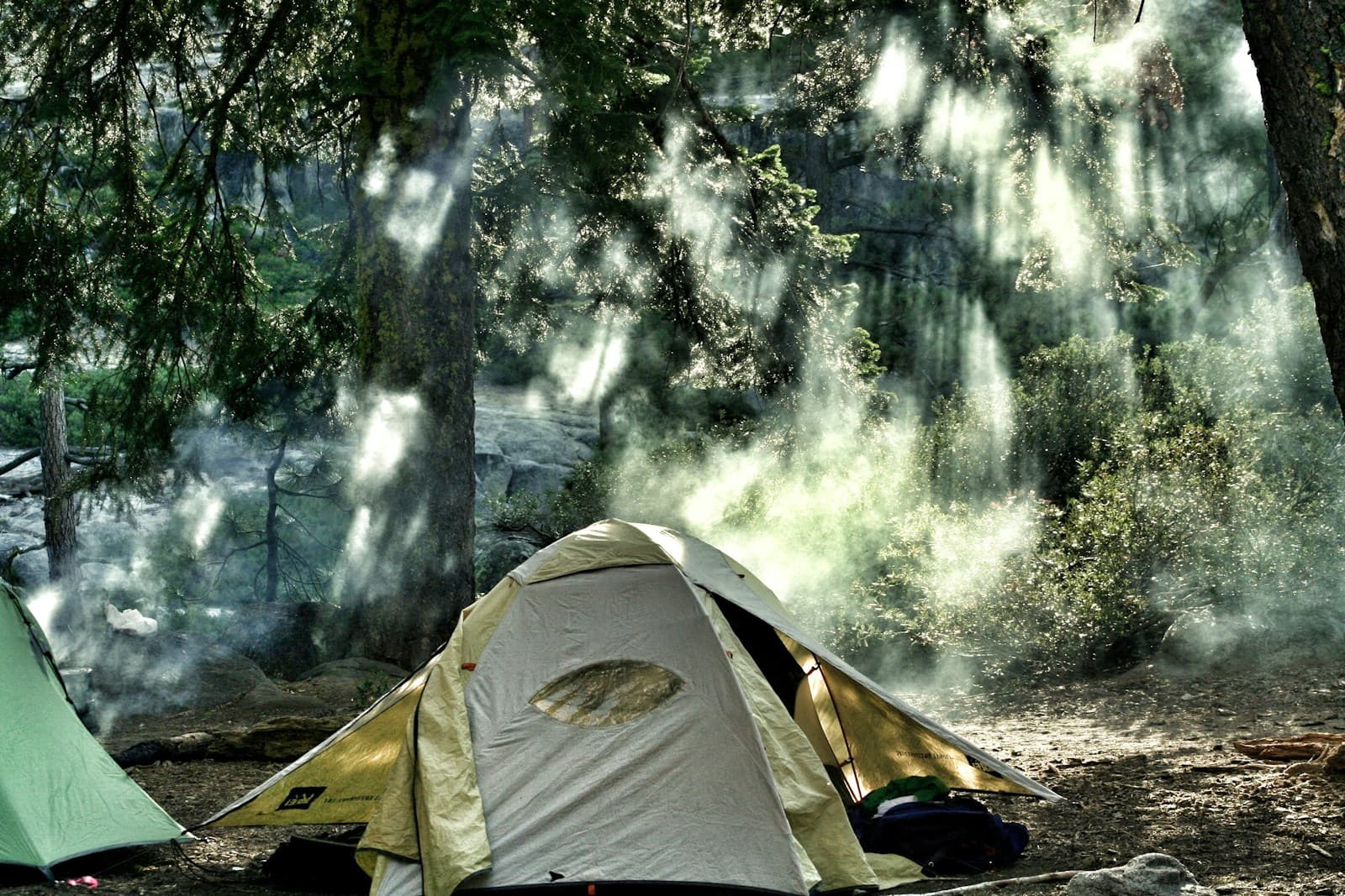 A yellow tent pitched among trees, with another tent partly visible beside it.