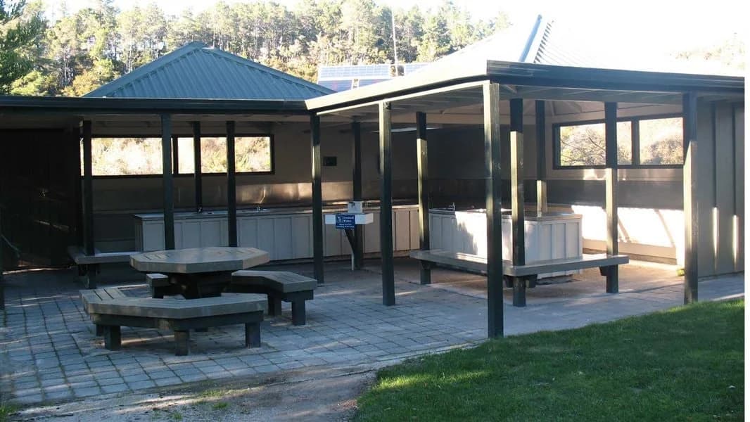 Open-sided campsite shelters and picnic tables beside a grassy area at Anchorage Campsite.