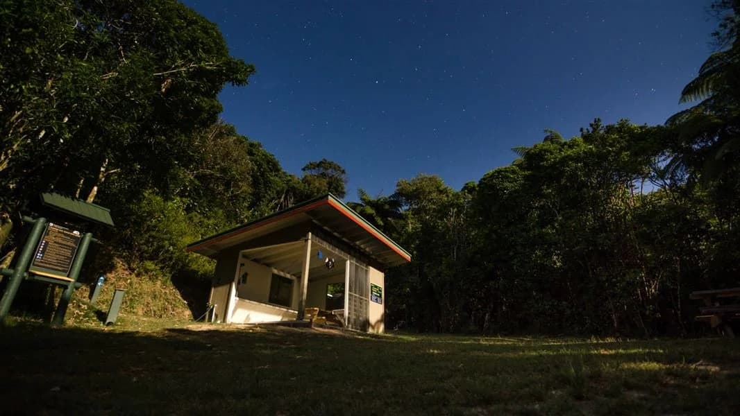 A small campsite shelter and picnic tables beneath trees at Camp Bay on the Queen Charlotte Track.