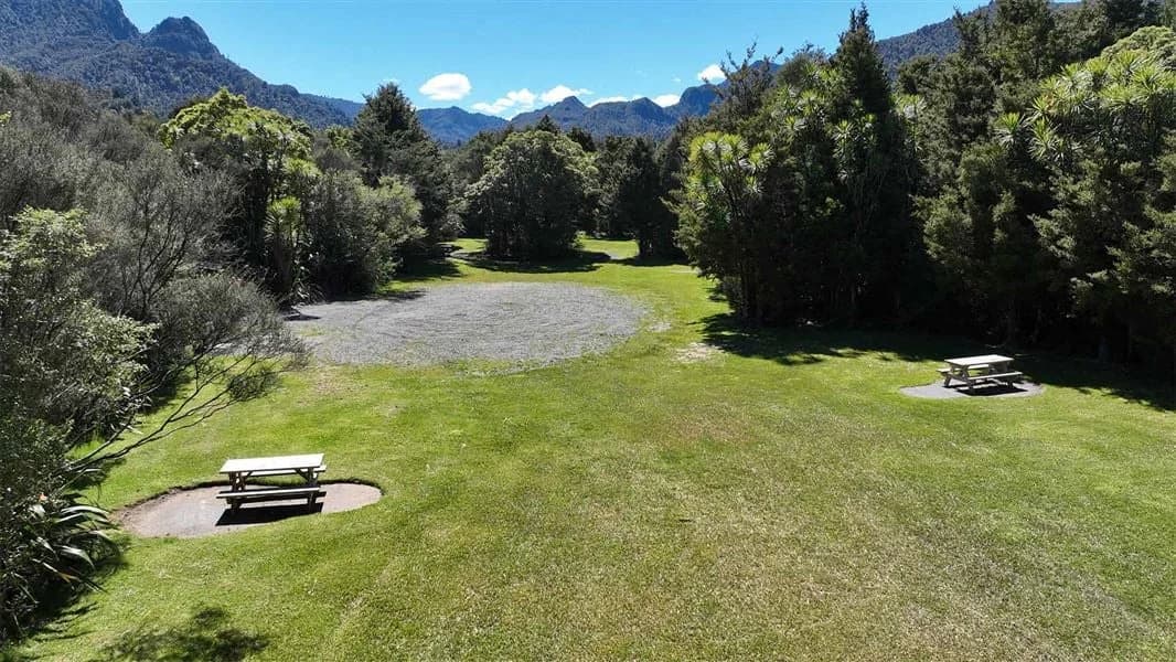 Grassy camping ground with picnic tables and a curved gravel road among trees at Catleys Campsite.