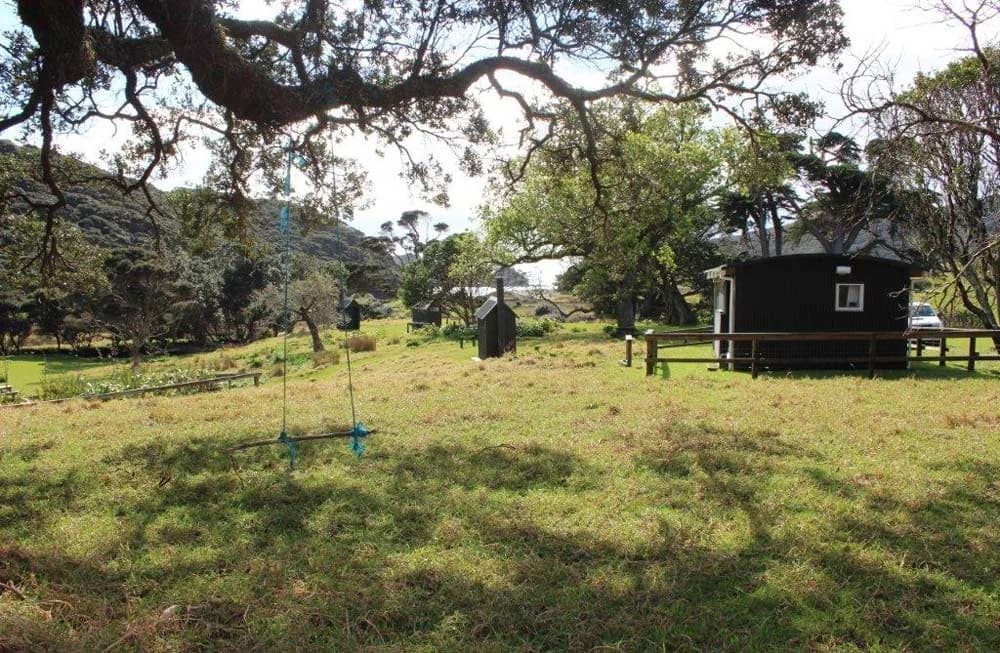 Grass camping ground, trees and a small service building at Harataonga Campsite on Aotea Great Barrier Island.