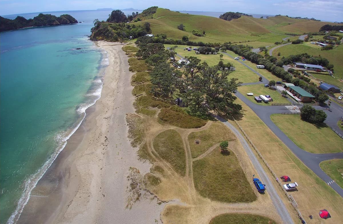 Aerial view of camping vehicles and grassy pitches behind the beach at Otamure Bay.