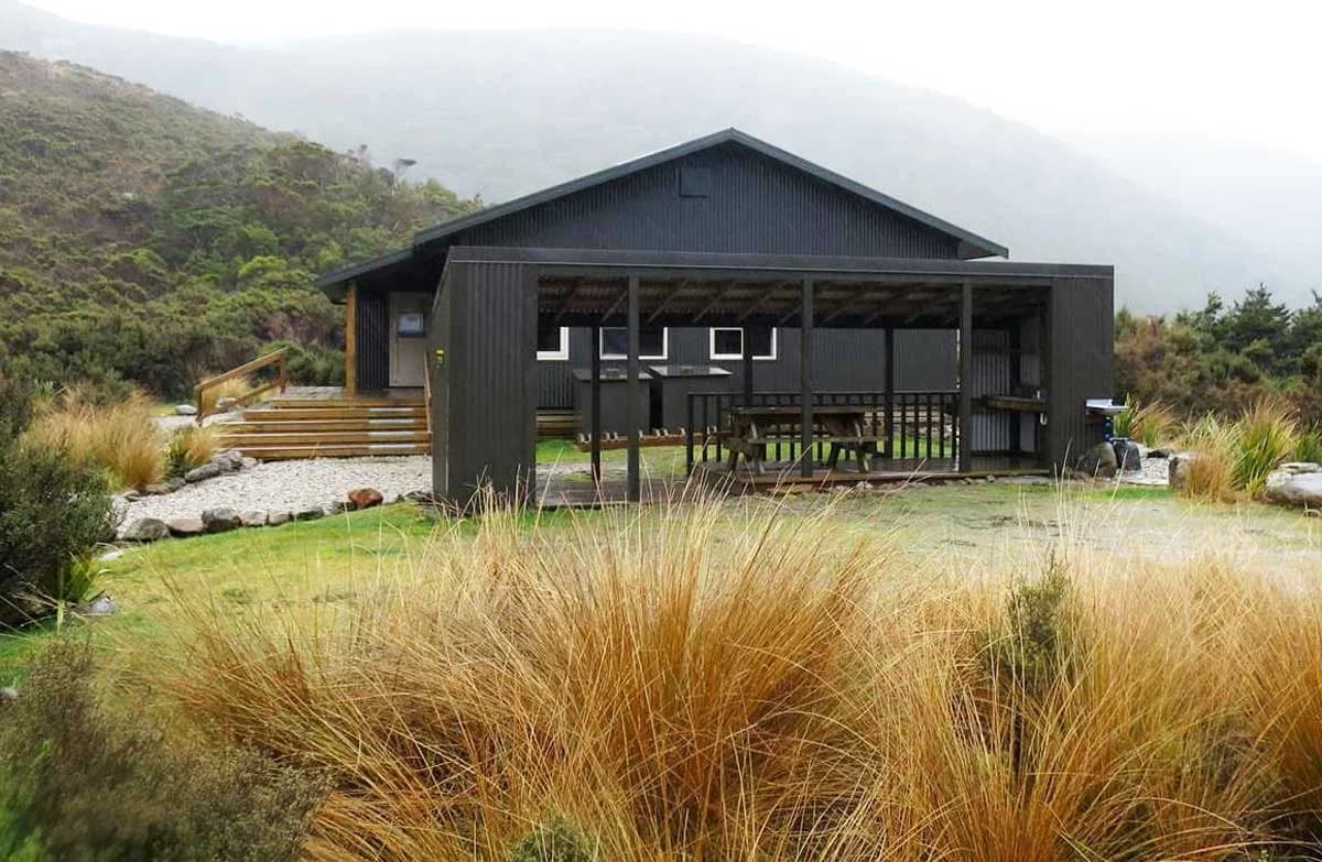 The open-front campsite shelter among tussock and grass at Perry Saddle Campsite on the Heaphy Track.