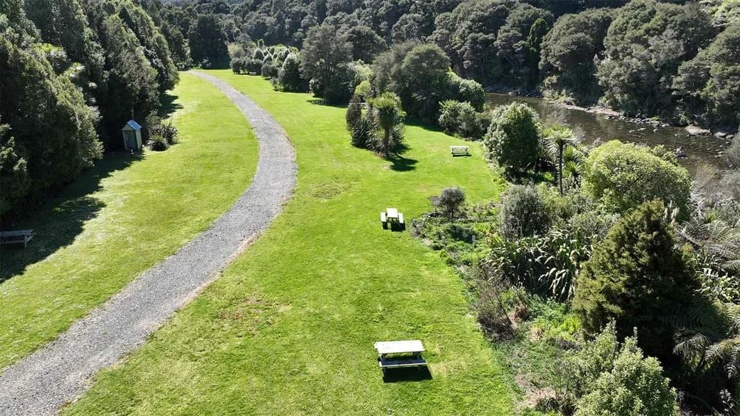 Aerial view of an elongated grass camping area, picnic tables and access road at Shag Stream Campsite.