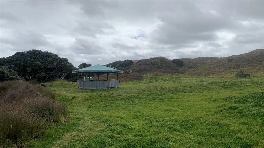 A roofed campsite pavilion on grass among coastal scrub at Twilight Campsite.