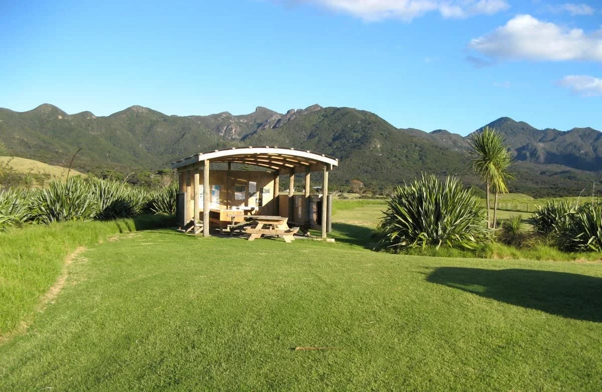 A picnic shelter on a broad grass camping area at Whangapoua Campsite on Aotea Great Barrier Island.