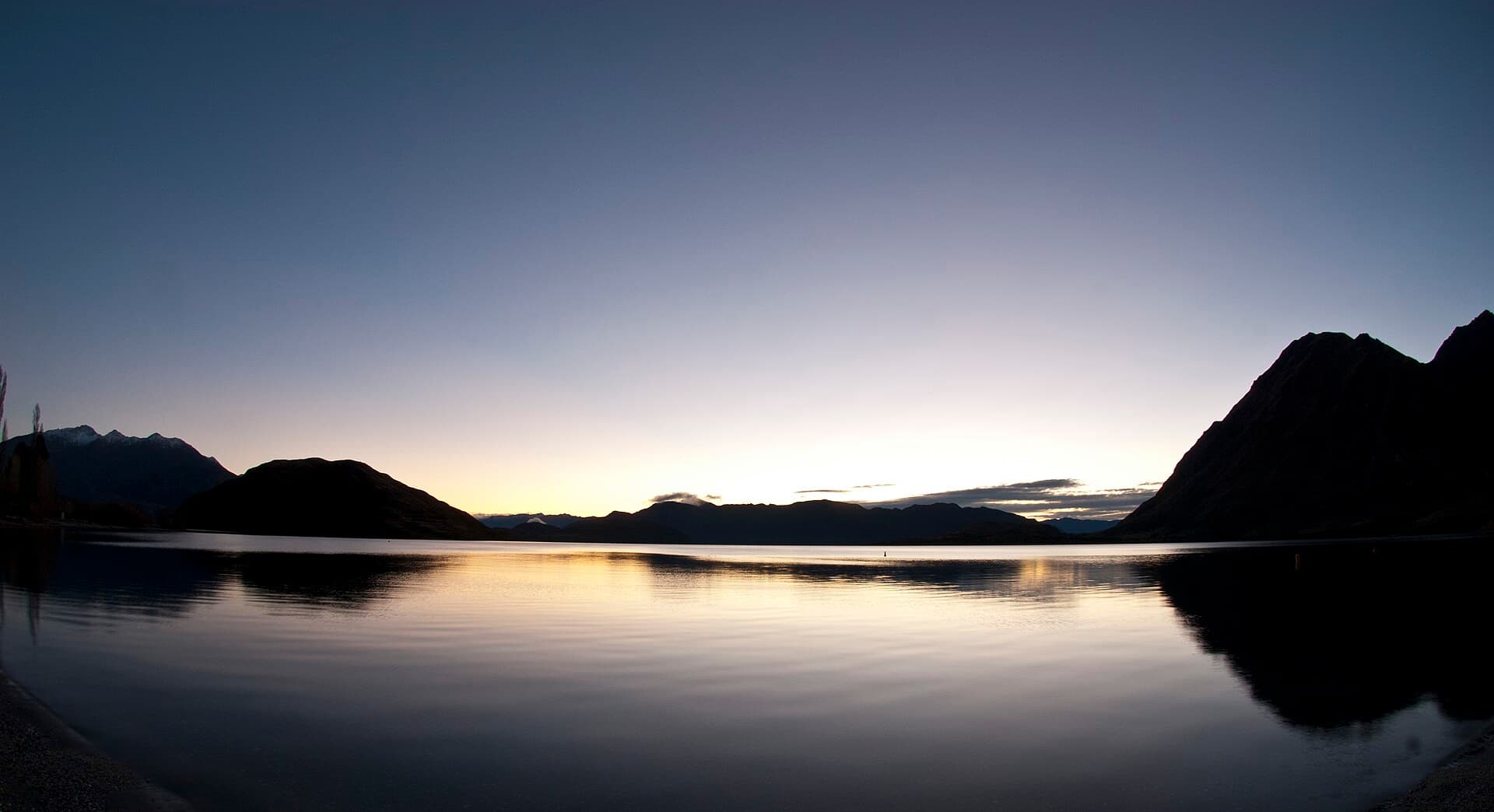 Glendhu Bay's still water beneath dark mountain silhouettes and a pale sky.