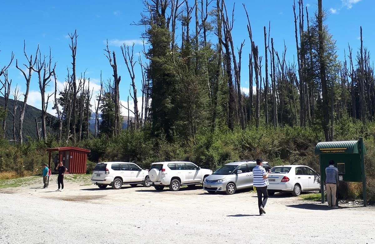 Camper registration kiosk, parked vehicles and a red service building on gravel at Diamond Lake Campsite.