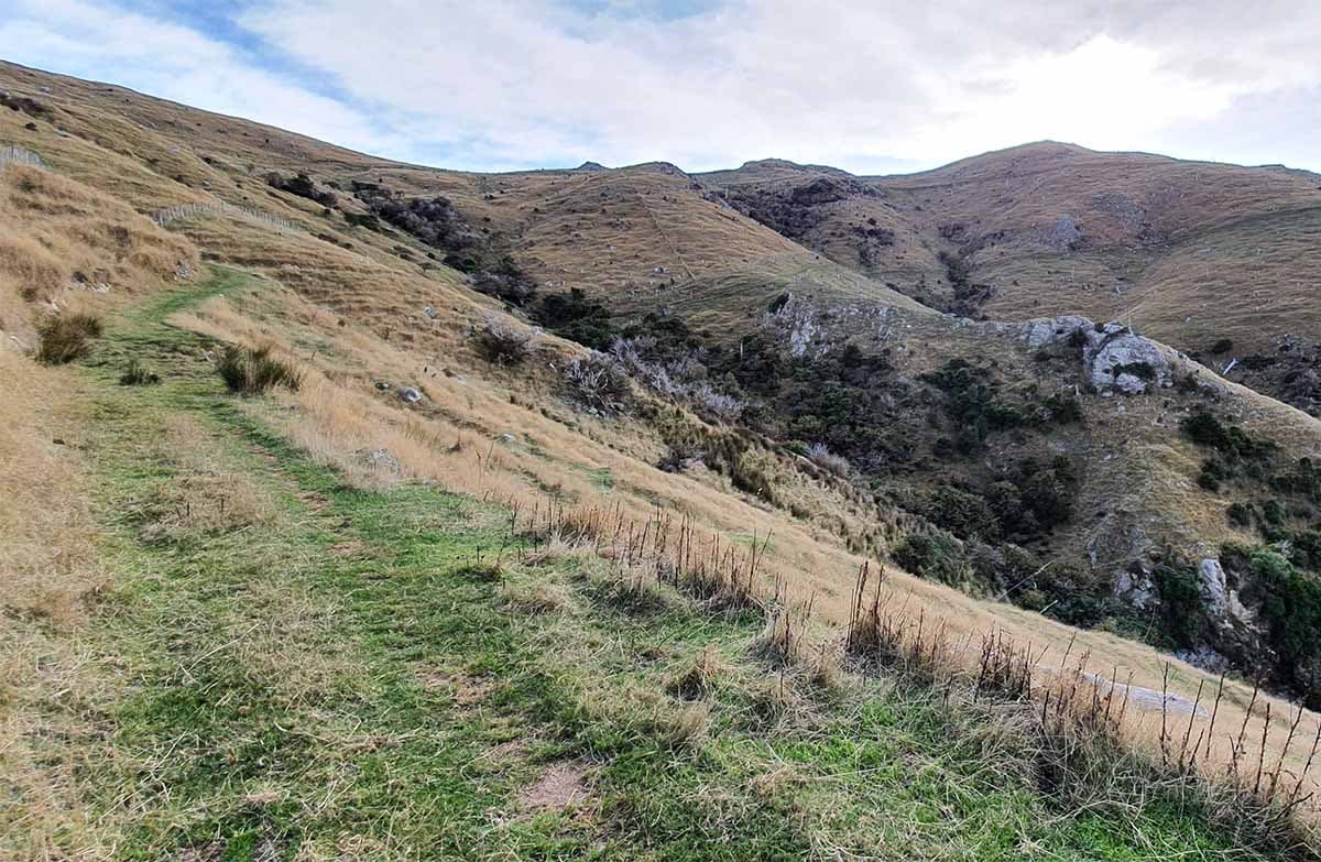 A grass covered track goes along the side of a hill higher and higher. A valley is seen to the right.