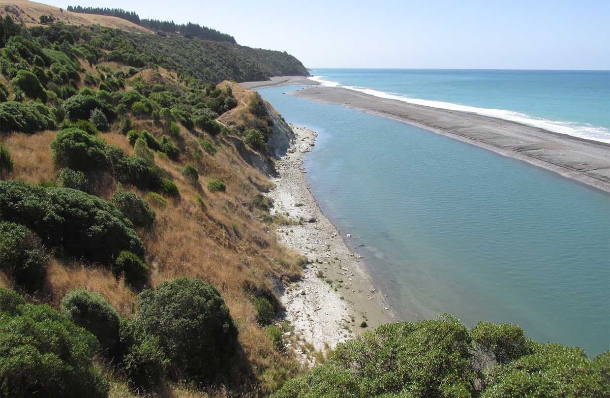 View from a high seaside cliff. There is a spit of land between two jutting pieces of land.