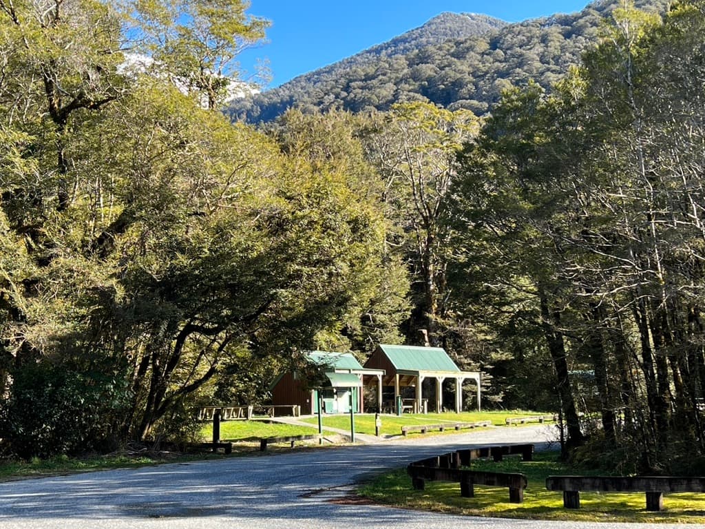 Green-roofed shelter and visitor buildings among trees beside a gravel road at Pleasant Flat.