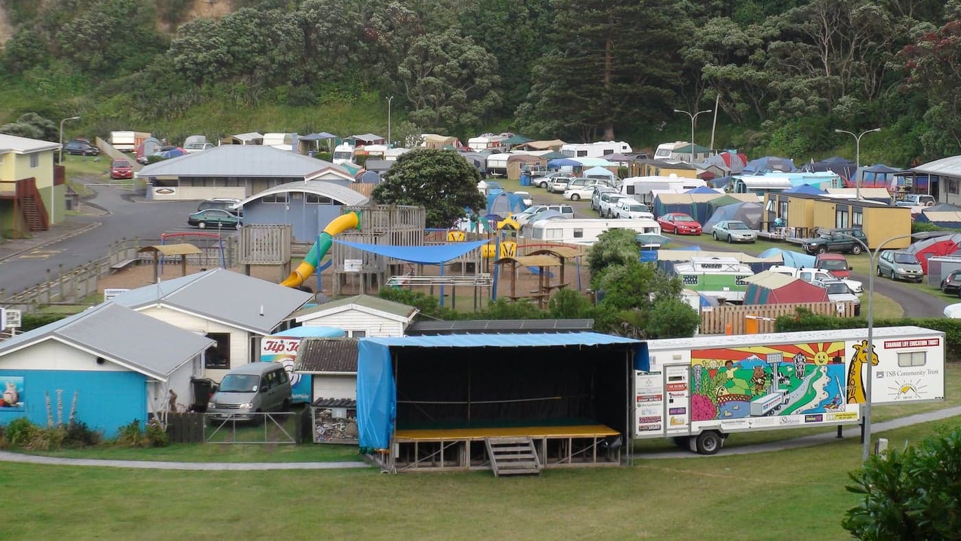 Tents, caravans, campervans and a playground at Opunake Beach Holiday Park, with an event stage in the foreground and trees behind the pitches.