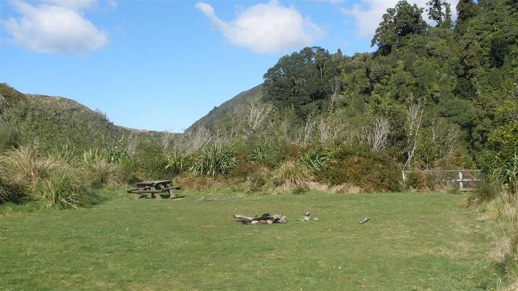 An open grassy camping area bordered by tall vegetation and hills at Waiohine Gorge Campsite.